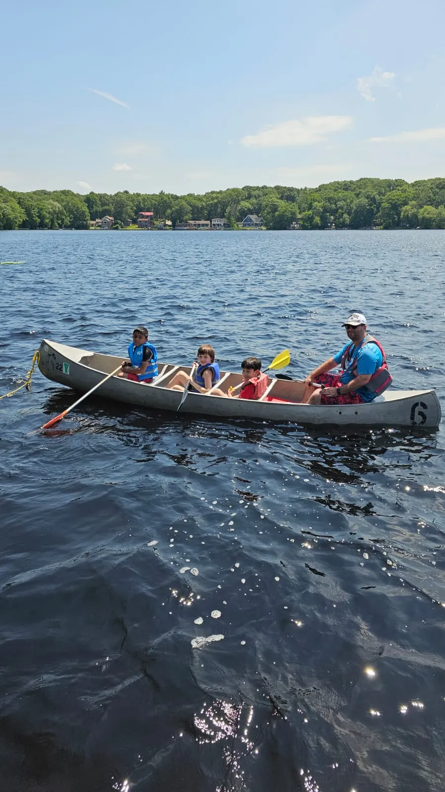 Three kids paddling in a canoe with a staff