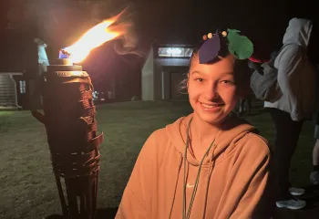 A female camper holding a tiki torch at the end of a Survivor themed Kids' Night Out.