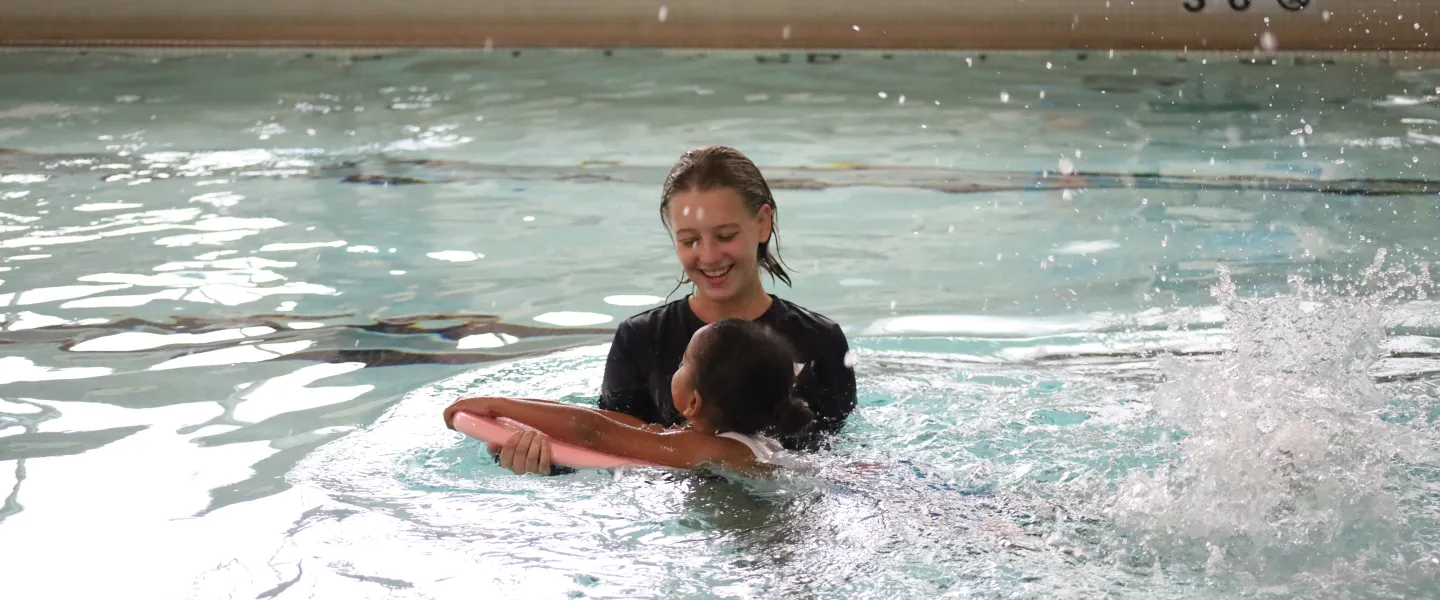 Female swim instructor teaching a girl how to swim with a kickboard