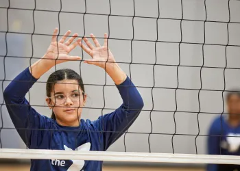 Girl with her hands up behind a volleyball net waiting for the ball