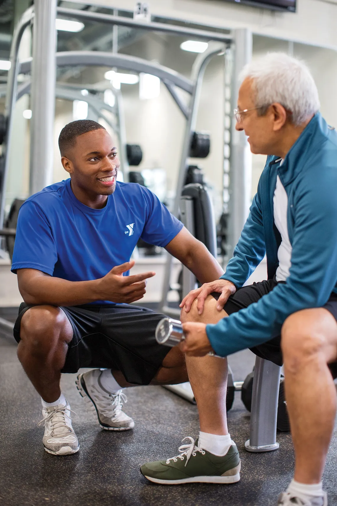 Male trainer sitting with male client holding a weight