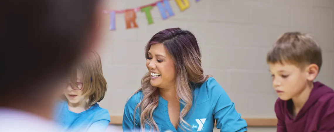 Staff sitting at table with kids with a "Happy Birthday" banner behind her