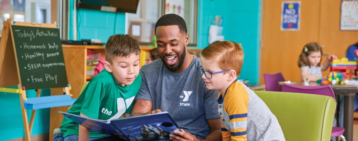 Two boys sitting with a male staff reading a book
