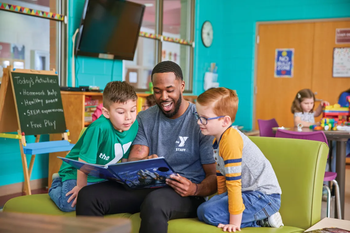 Two boys sitting with a male staff reading a book