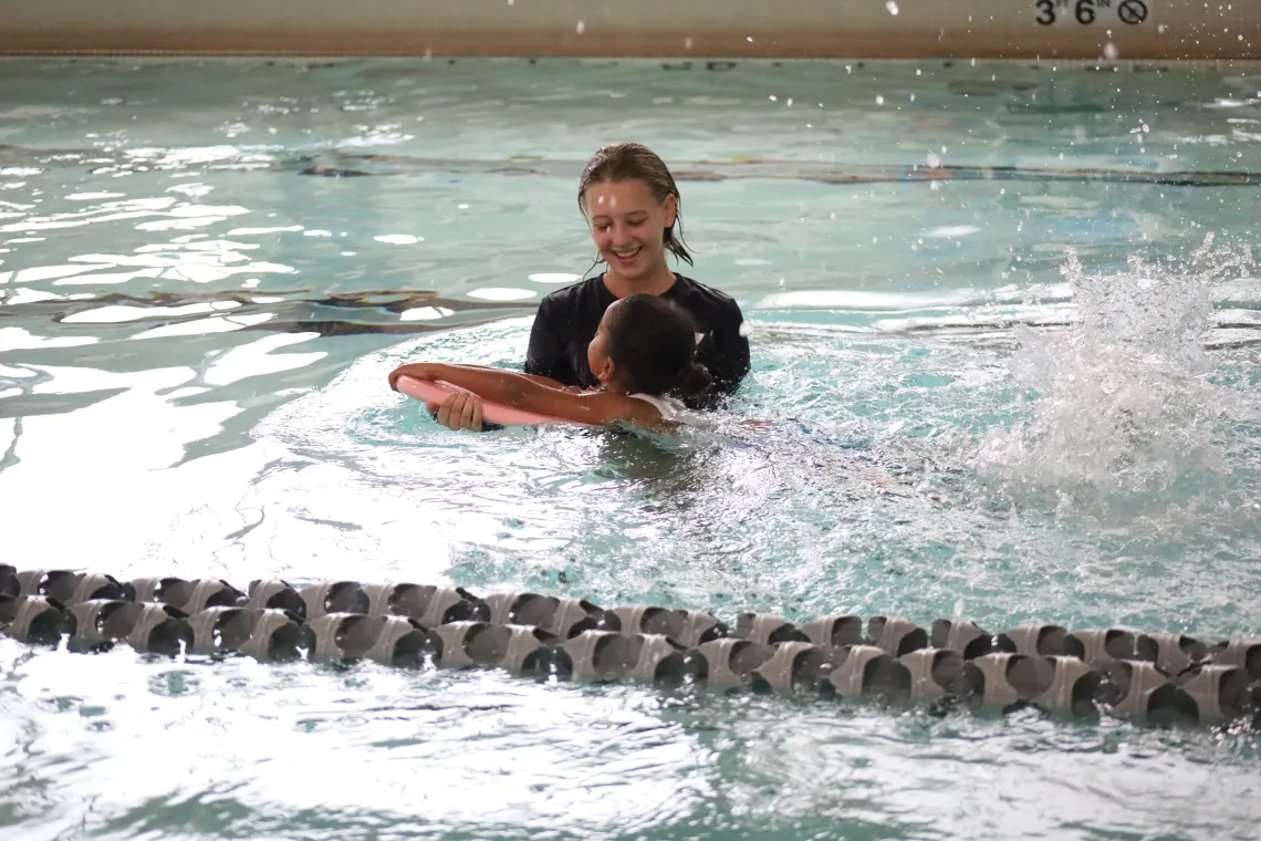 Female swim instructor teaching a girl how to swim with a kickboard