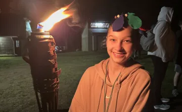 A female camper holding a tiki torch at the end of a Survivor themed Kids' Night Out.